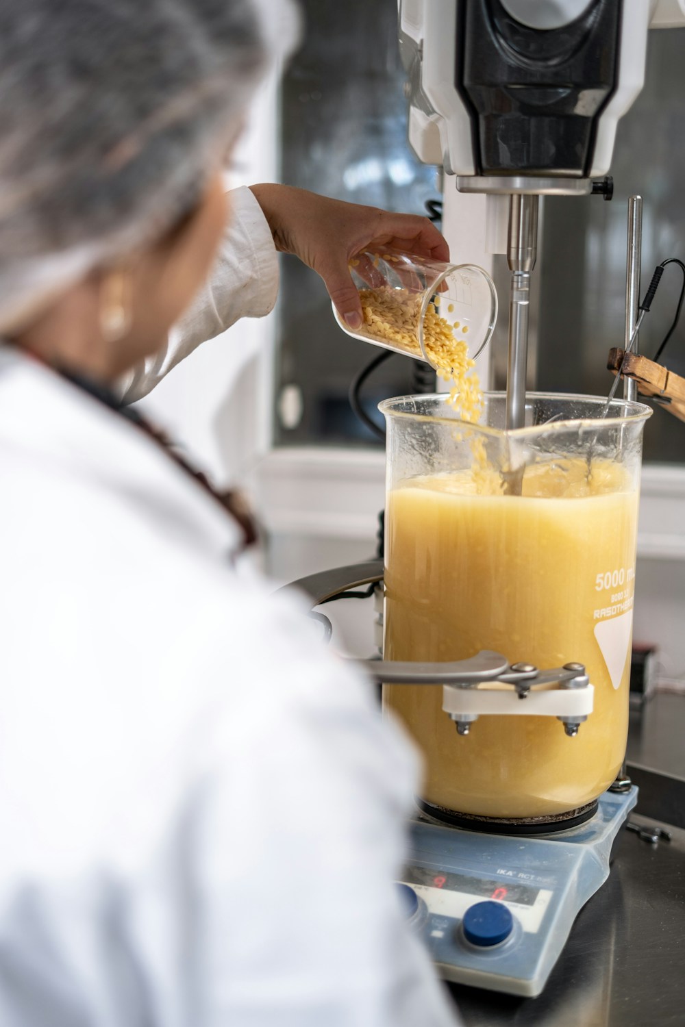 Een laboratoriummedewerker voegt ingrediënten toe aan een mengvat